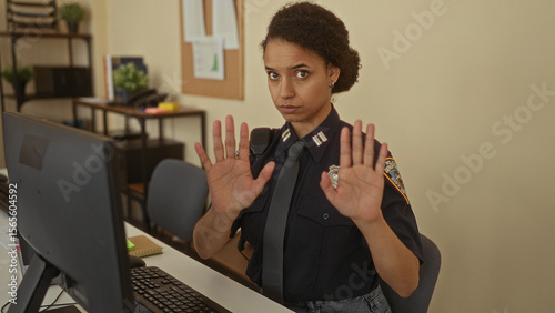 Photos Young woman police officer holds palms forward in a calm gesture at station desk; calm professionalism