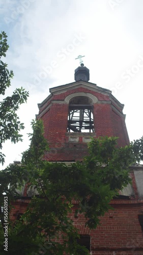 The bell tower of a derelict Orthodox church, constructed of brick, with a lopsided cross at its summit. vertical