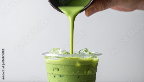 A fresh Matcha beverage is being poured over ice. The vibrant green liquid contrasts with the clear ice cubes