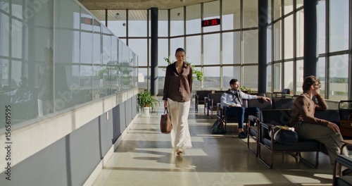 An elegant young woman walks through the lobby at the airport. People are waiting for a flight sitting in chairs