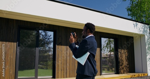 A stylish business man takes pictures of a house on a mobile phone