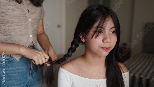Schilderij op canvas Sister braiding hair of her younger sibling, creating a beautiful hairstyle in a