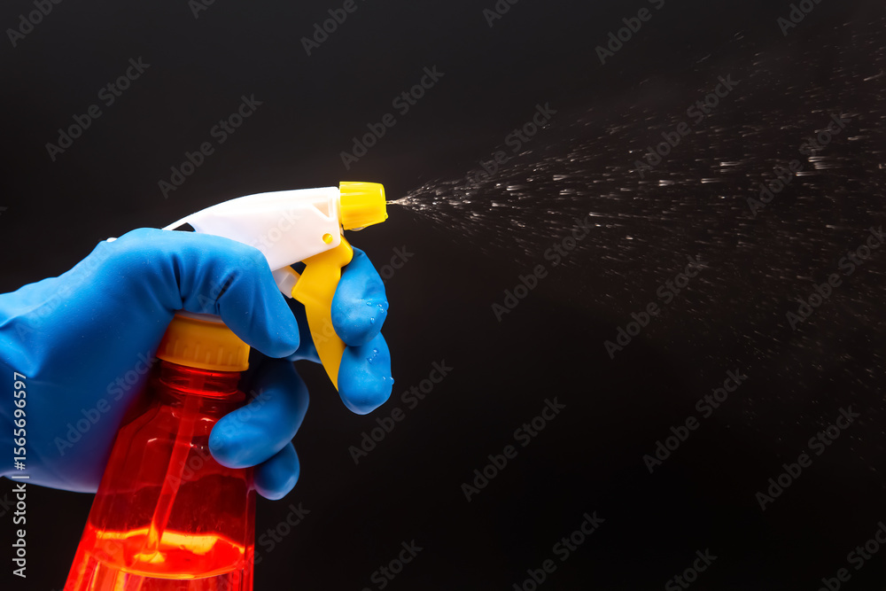 Naklejka premium A gloved hand activates a red spray bottle with a yellow nozzle, releasing a fine mist on a black backdrop, perfect for cleaning product ads or sanitation themes.