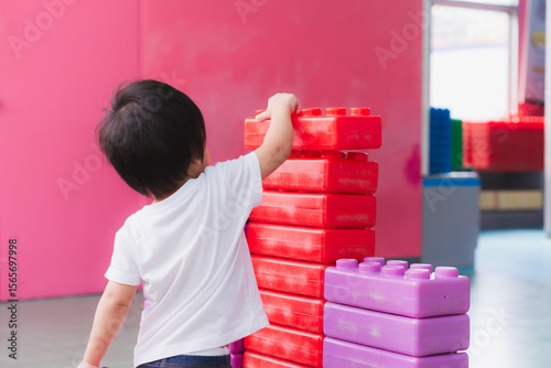Rear back view. Asian little Boy having fun playing with colorful blocks indoors playground. Child creating new cities with toys. Imagination and learning. 2 year old son.