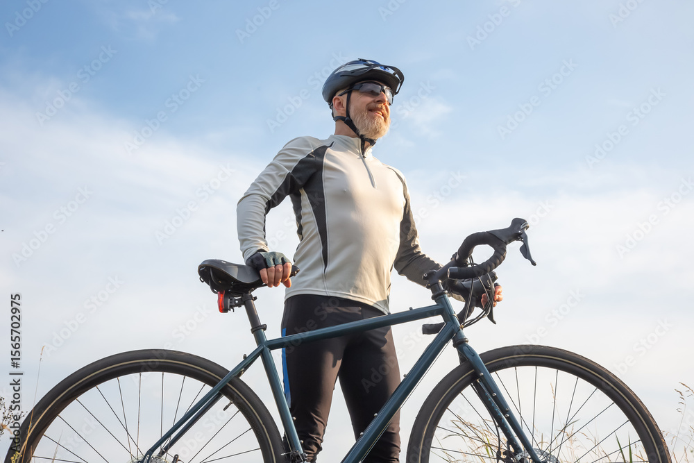 Naklejka premium Bearded man cyclist stands with a bike against the blue sky. cycling and health hobbies