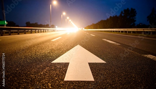 Road Ahead: White arrow on asphalt road at night, guiding toward a bright future. photo