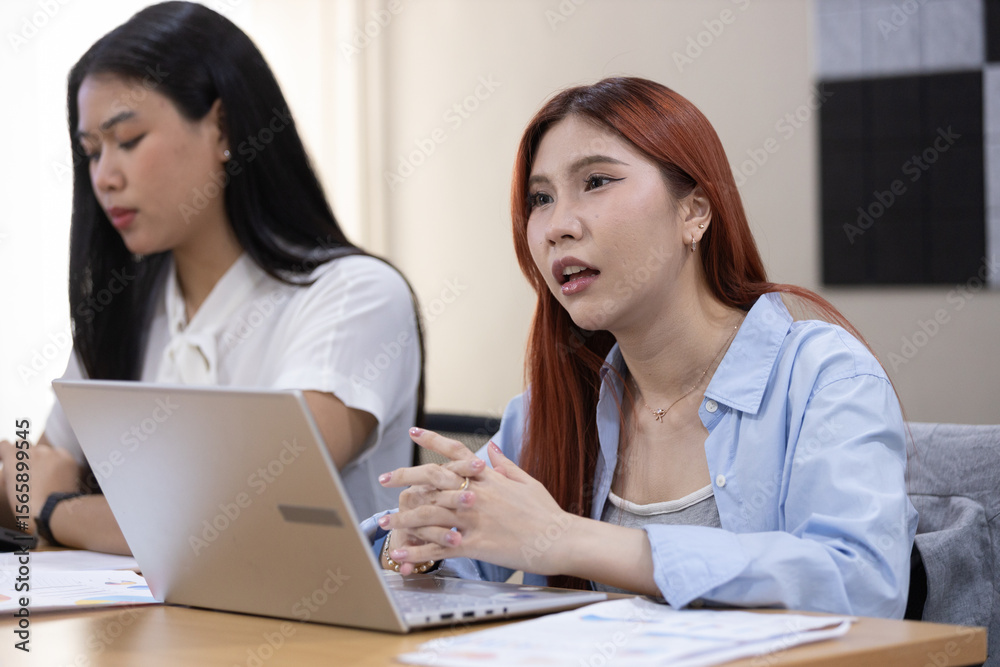 In a contemporary office environment, two women converse intently at table about work. In a contemporary office environment, two women converse intently at table about work.