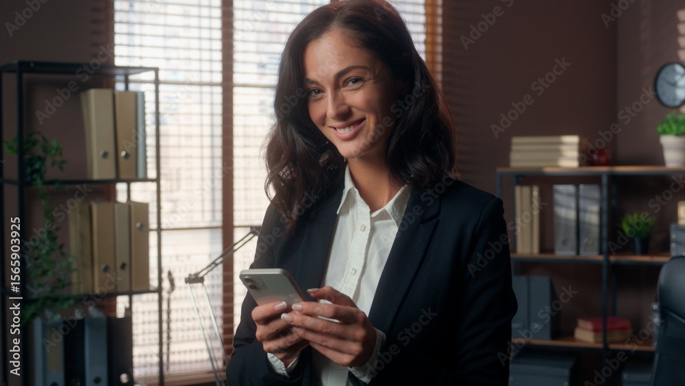 Fototapeta premium Caucasian woman holding mobile phone smartphone cellphone online winking looking at camera female girl businesswoman business office smiling manager employer friendly blink happy worker indoor texting