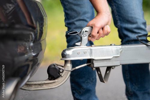 Attach a trailer to the car close up. Locking the lever of the Hitch coupling to connect to the hitch ball. Usage of the tow hook below the rear bumper.