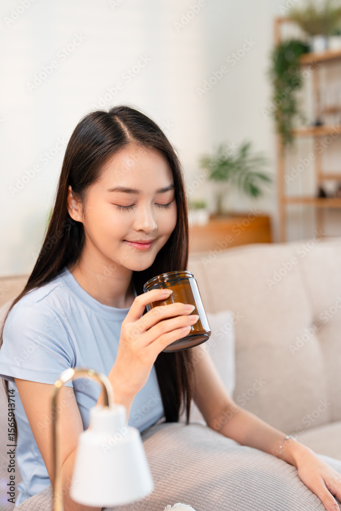 Young woman relaxing sitting on sofa smelling aromatic scented candle at home. Young woman relaxing sitting on sofa smelling aromatic scented candle at home.