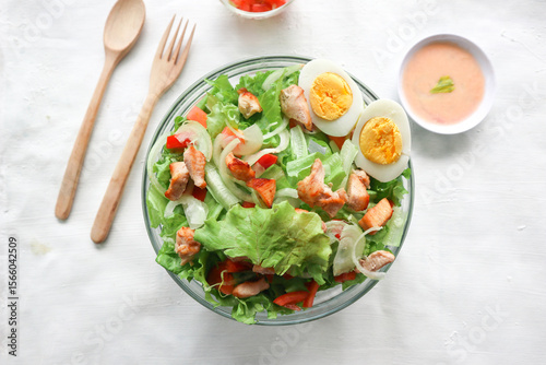A cesar salad bowl filled with lettuce, tomatoes, egg and chicken. The salad is served in a clear glass bowl