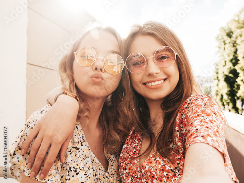 Two young beautiful smiling hipster female in trendy summer sundress.Sexy carefree women posing on the street background in sunglasses. Positive models having fun and hugging