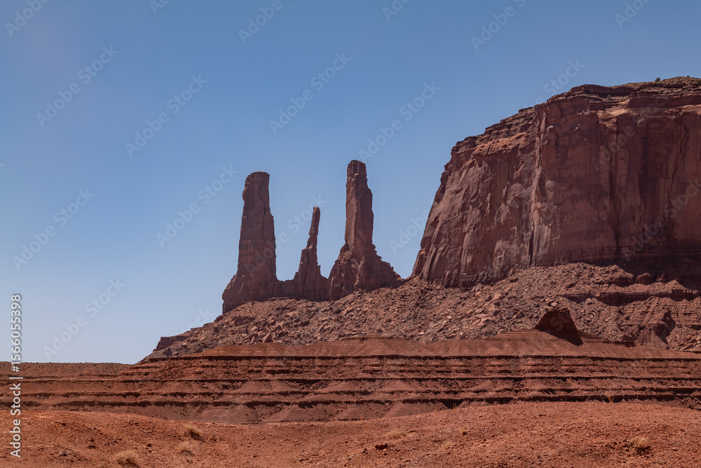 Fototapeta premium The Three Sisters spires in Monument Valley on the Colorado Plateau, Arizona. De Chelly Sandstone with Organ Rock Formation / Shale. A mesa is a flat-topped mountain or hill. Mitchell Mesa. Pinnacle