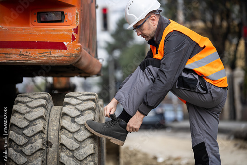Construction worker adjusts boots before operating heavy machinery at a worksite in the city