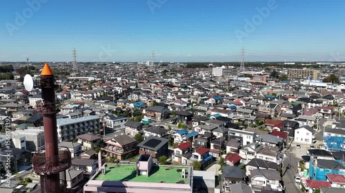 Forward moving aerial drone shot flying over a dense Japanese suburban residential area, showcasing a vast expanse of tightly packed houses with varied rooftops, narrow streets