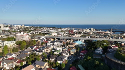 An breathtaking aerial drone shot glides forward over a vibrant coastal Japanese town. The scene captures a harmonious blend of traditional and modern residential architecture 