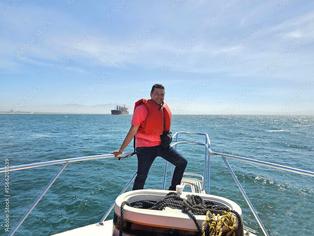 Fototapeta premium Dark-skinned Latino adult man wearing a life jacket enjoys a boat tour with ocean views during his vacation