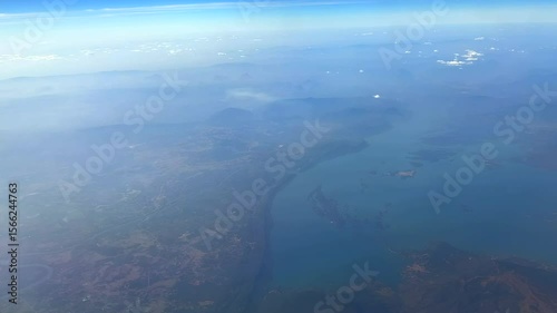 Plane flying over coastal landscape. Plane window view of cloudscape. Panoramic view from a plane window.