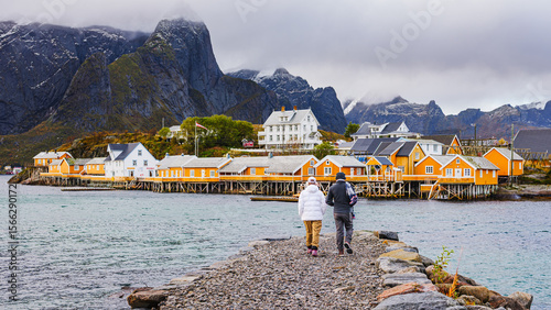 Fotografie Couple walking to traditional rorbuer cabins in Sakrisøy, Lofoten Islands, Norwa