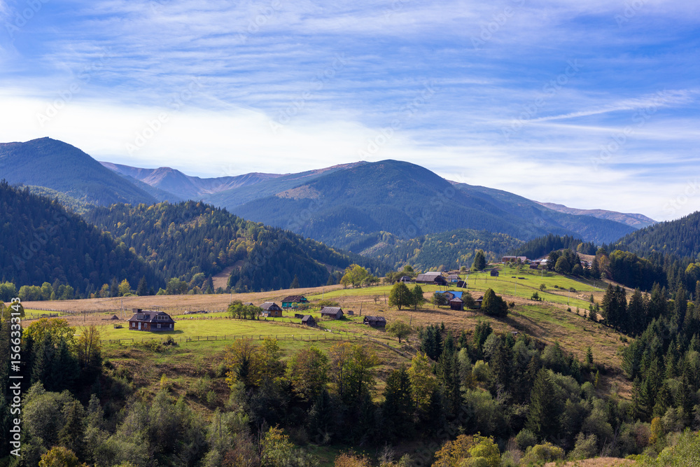 Obraz premium Breathtaking Scenic View of the Ukrainian Carpathians Capturing a Serene Village Surrounded by Lush Green Hills and Colorful Autumn Foliage Under a Clear Blue Sky