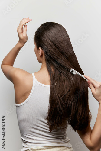 Hair care, grooming, brushing, beautiful hair, women s hairstyles A young woman with long, straight hair is combing her hair against a plain white background, showcasing a healthy looking hairstyle