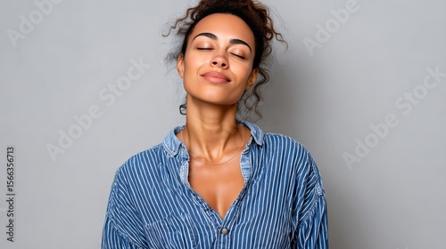 Woman is smiling and looking at the camera. She is wearing a blue shirt with white stripes