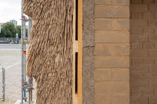 Close-up of a sustainable building wall cross-section showing natural insulation materials including reed, hemp, and clay bricks, at a construction site