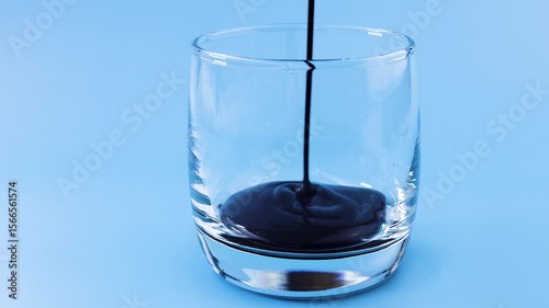 View dark chocolate sauce pouring into glass on pale blue background. Food and drink concept.