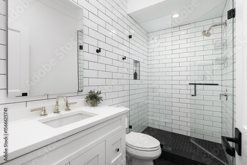 A white bathroom with subway tile walls, gold faucets, and black square tile flooring.