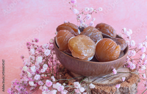 Castañas glaseadas (marrón glacé) en cuenco de madera con flores rosas sobre fondo rústico