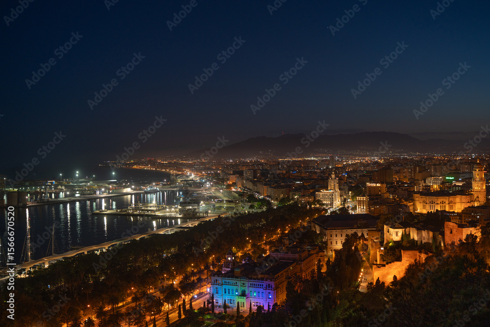 Fototapeta premium Sparkling Malaga Port and Illuminated Cityscape at NightAn enchanting night view of Malaga's illuminated port, featuring the glowing lighthouse, bustling promenade, and a vibrant city a