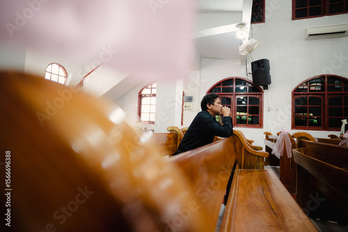 Contemplative person in quiet church interior with wooden pews and stained glass windows