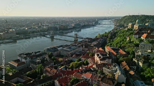 Sideward drone video at sunrise from Fisherman’s Bastion, centered on Chain Bridge and Danube River with Buda Castle, rooftops, and historic Buda-side architecture in view.  
