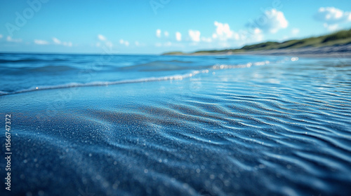 Gentle waves lapping sandy beach, sunny sky, distant dunes