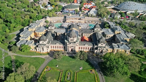 Still aerial video with top-angled view of Széchenyi Thermal Bath centered symmetrically, showing front garden, parts of the Capital Circus, and the Budapest Zoo in City Park during morning light.  