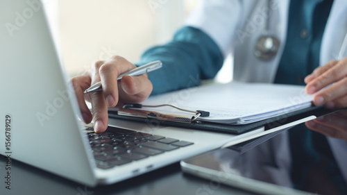 Doctor working on laptop computer and preparing patient's information for meeting with medical team. Doctor doing medical health record and medical prescription, insurance claim form