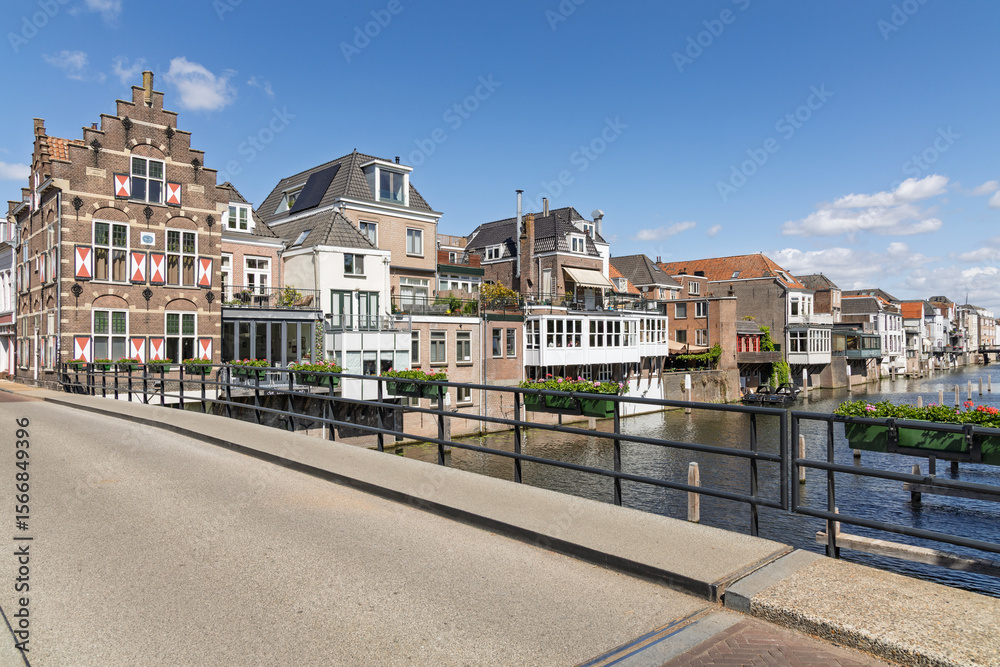 Obraz premium Charming traditional Dutch houses line the historic canal in Gorinchem, adorned with flower boxes, under a bright blue sky.