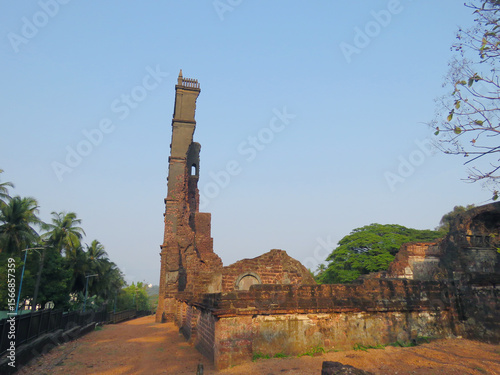 Ruins of the Church of St. Augustine tower in Old Goa, India, with weathered laterite brick walls and a lone chimney silhouetted against a clear sky, evoking centuries of colonial history and architec