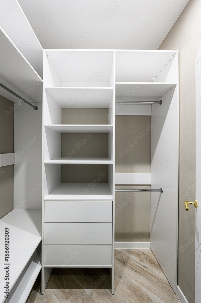 Fototapeta premium well-lit, open white closet with shelves, drawers, and hanging rods. The interior is beige. Parquet flooring is visible at the bottom