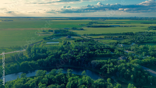 Epic aerial photo of a vast river valley with lush forests, green farmland, and a city skyline on the distant horizon at sunset.