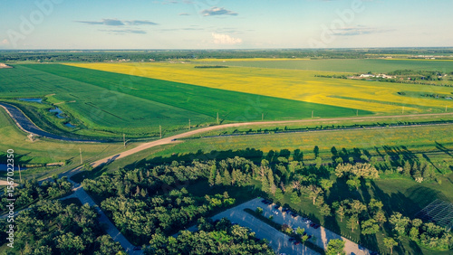 Aerial view of a rural park beside vast, contrasting green and yellow farm fields at sunset.