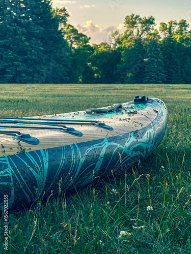 An inflatable kayak with a tribal pattern rests on a grassy lawn. Summer outdoor adventure and recreation concept.