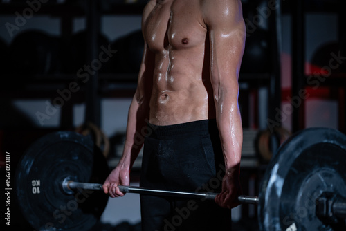 Sweaty bodybuilder lifting weights in dark gym