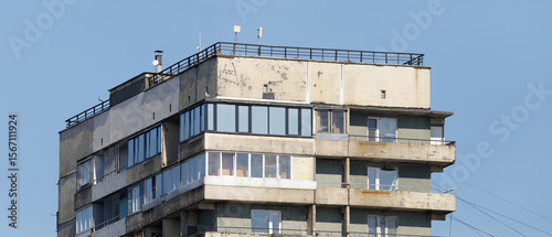 Close-up of the upper floors of a Soviet-style apartment building, showing aging balconies, rooftop antennas, and weathered facade.