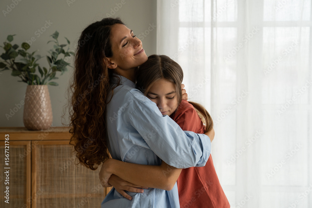 Obraz premium Young loving mother hugging her teenage daughter, mom demonstrating unconditional love for child, mommy cuddling supporting upset teen girl while spending time together at home. Mother-daughter bond