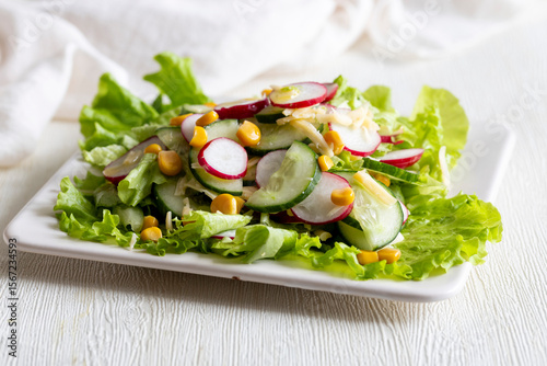 Vegan spring organic salad with fresh radish, cucumber, sweet corn and lettuce leaves with olive oil on white square plate. Healthy diet