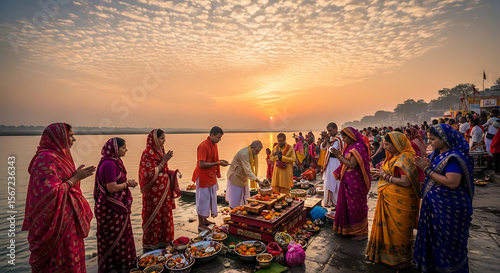 People gather at a riverbank for a religious ceremony during sunrise, with offerings and prayers.