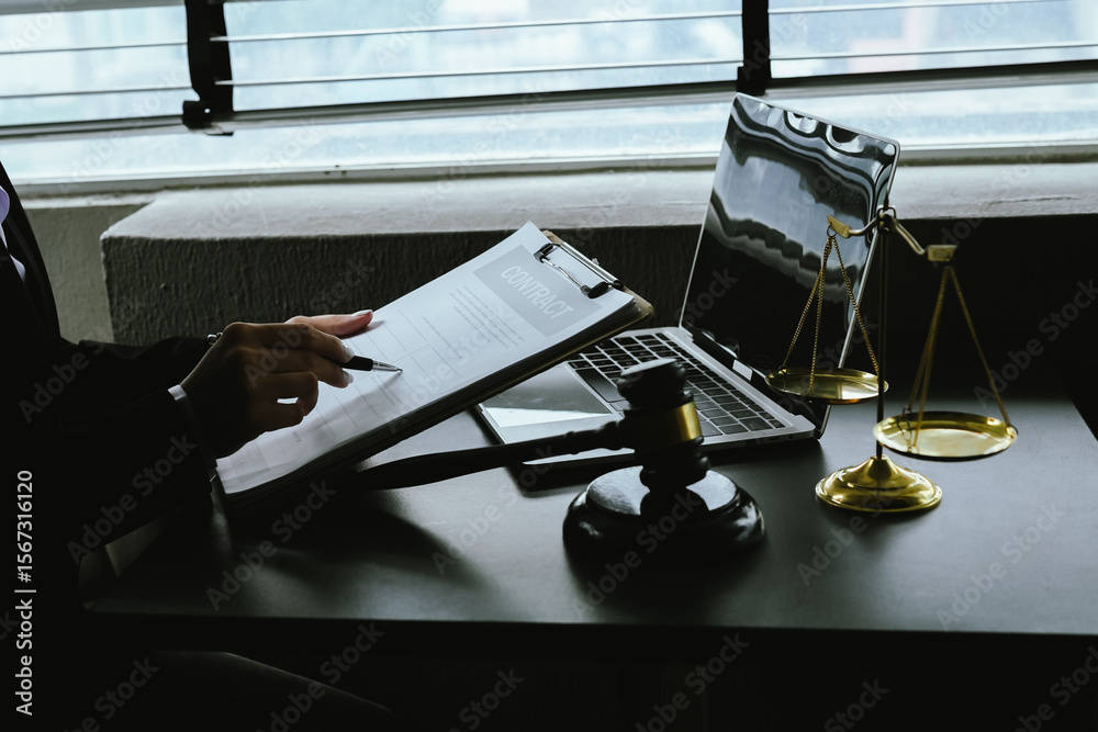 Obraz premium A gavel rests on a legal desk with blurred background of a professional signing documents, symbolizing justice, legal process, court authority, and formal legal consultation setting.