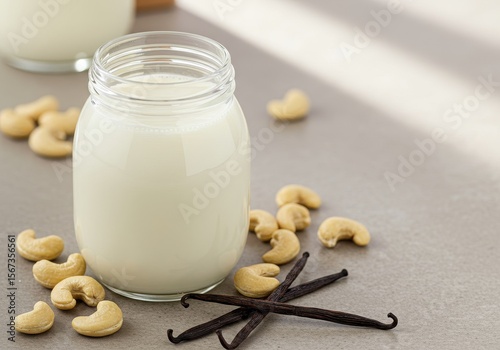 Glass jar of creamy cashew milk with cashews and vanilla beans on a stone countertop in soft natural light