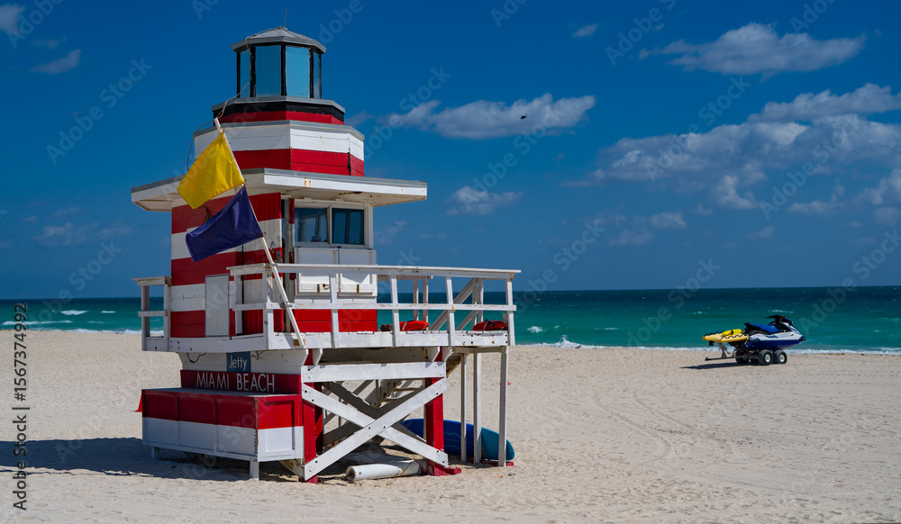 Fototapeta premium Miami Beach lifeguard at the summer beach. Tourism on South Miami Beach. Sky above lifeguard tower in Miami. Iconic lifeguard tower on sand in Miami. A symbol of Miamis coast.
